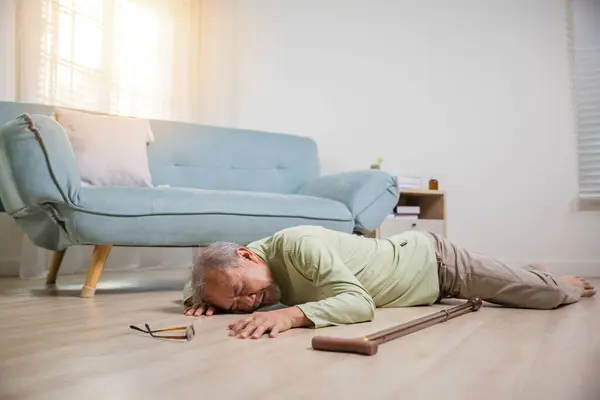 Elder man falling on the floor alone with walking stick on living room at home, Older senior man headache lying on the floor after falling down, Health care and medicine concept