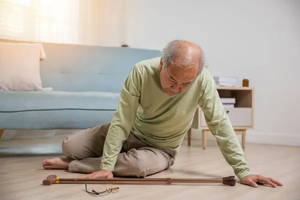 Asian senior man falling down lying on floor at home alone with wooden walking stick in living room, Elderly man headache after fall down, Health care and medicine concept