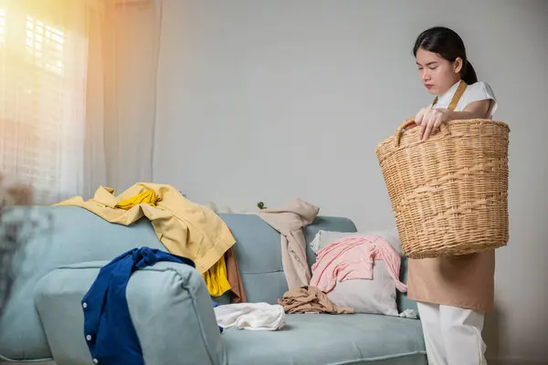 Asiatische Hausfrau Hält Korb Mit Haufen Unterschiedlicher Kleidung Auf Sofa — Stockfoto