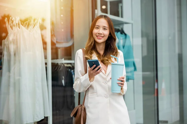 Coffee break in the city ,young woman holding a tumbler mug and smartphone in front of an office building. Hot beverage and digital communication is her convenience.