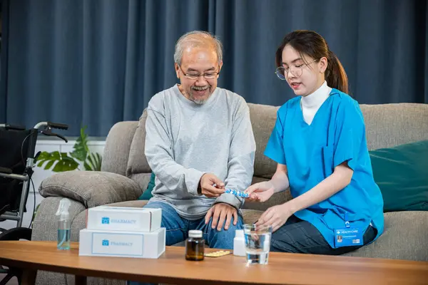 Asian nurse with physician explaining prescription medicine to attentive senior man at home, Doctor woman explain dosage pill old man, Healthcare worker caregiver visiting in house in living room
