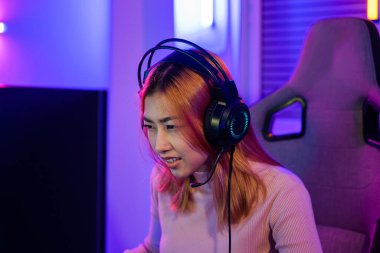Young player woman wearing gaming headphones intend to do playing live stream games online at home, Happy Gamer endeavor plays online video games tournament with computer desktop with neon lights