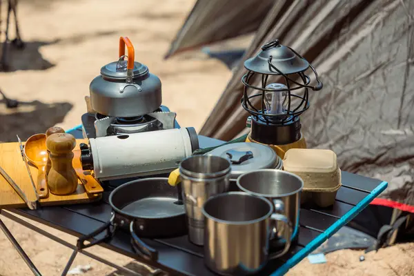A picturesque morning at the campsite, essential cooking equipment, kettle, pot, pan, gas stove, and camera, set up by the tent. Camping in nature has never been more delightful.