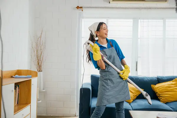 Maid musical touch, Asian woman enjoys vacuum guitar husband playful twist. Singing dancing happily while cleaning. Music-infused service brings excitement to housework. Cleaning is fun