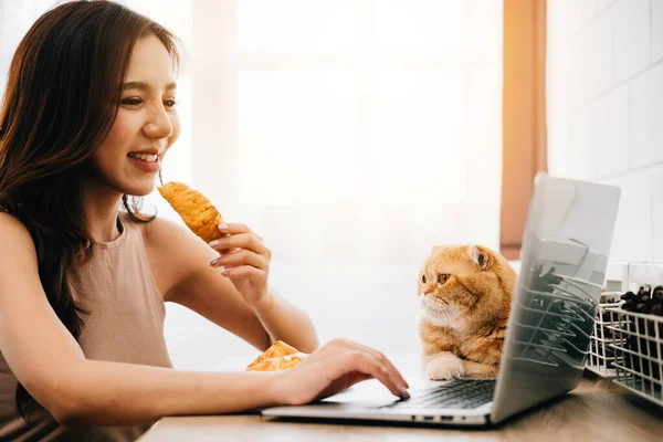 In this heartwarming home office scene, a woman balances her work on a laptop with cuddles from her lovely Scottish Fold cat at her desk, emphasizing the harmony of work and togetherness.