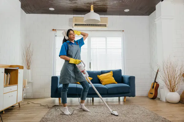 Domestic joy, Asian housewife sings dances with mop mic in hand. Joyful occupation filled with music humor. Modern housework fun. Give me a smile, maid dancing having fun