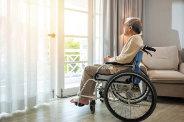 Yalnız, yaşlı, düşünceli, üzgün yaşlı bir adam huzurevinde yatak odasının pencerelerine bakıyor. Asyalı, yaşlı bir adam sakat.