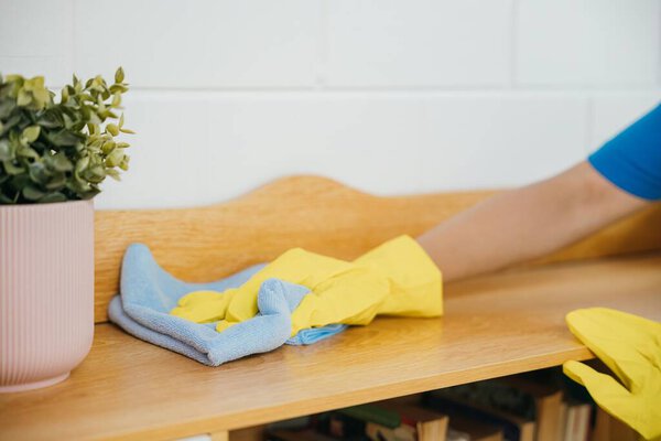 A cheerful housewife in yellow gloves diligently cleans the table. Her commitment to home hygiene and cleanliness reflects in her routine cleaning tasks. The woman is.