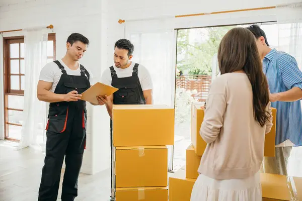 Couple checks moving checklist worker holds cardboard box. Professional movers ensure smooth relocation service. Teamwork and efficient home moving displayed. Movind Day