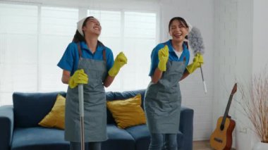 Ev işleriyle uğraşan iki üniformalı kadın profesyonel temizlik malzemesi kullanarak kirli bir odada dikiliyorlar. Gülümsemeyle mobilyaları temizleyen ve oturma odasının saflığını sağlayan bir takım olarak çalışırlar..