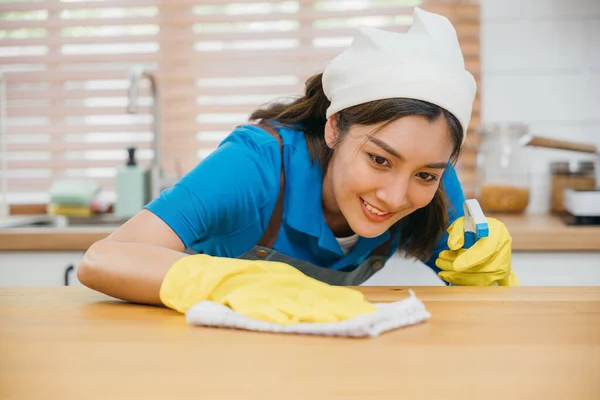 Asian cleaning service professional uses liquid spray to clean wooden kitchen counter. Housekeeping service ensures hygiene and cleanliness at home. Clean disinfect home care. maid household job.