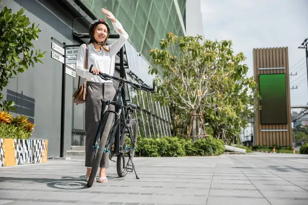 A fashionable biker in the city embraces hot summer season using her hand to shield from sun. Her cheerful smile adds a touch of beauty to bright urban environment. where travel meets happiness.