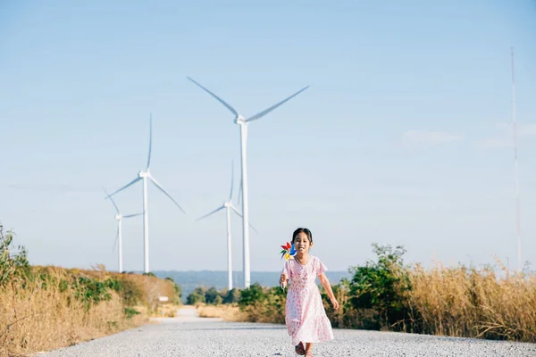 Little girls playful learning near windmills holding pinwheels with joy. Embracing wind energy education in a cheerful clean electricity generating wind turbine landscape.