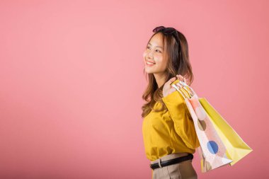 Gülümseyen ve heyecan dolu alışveriş torbaları taşıyan güzel bir Asyalı genç bu stüdyoda pembe bir arka planda çekilen neşeli alışverişin somut örneğidir. Çok mutlu..