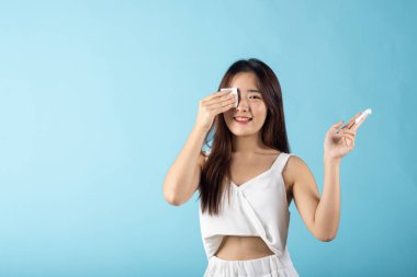 Yüz Bakımı Derisi 'nden. Kozmetik makyaj malzemelerini çıkartan Asyalı güzel bir kadın. Pamuk yüz temizleme diski, stüdyo resmi. Mavi arka planda izole edilmiş.