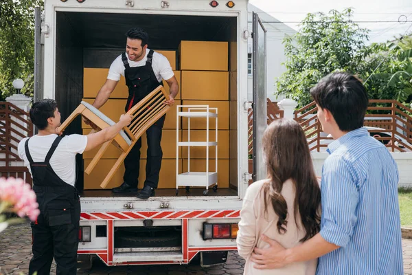 A couple benefits from a professional moving service for their new home. The team works together unloading and lifting cardboard boxes during the delivery process. Moving Day Concept