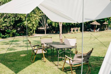 Açık hava pikniğinizi yaz kampı çadırı, masa ve sandalyelerle kurun. Bu banliyö terası, doğa dolu bir kutlama için mükemmel bir gölgelik ve rahat bir yer sunuyor..