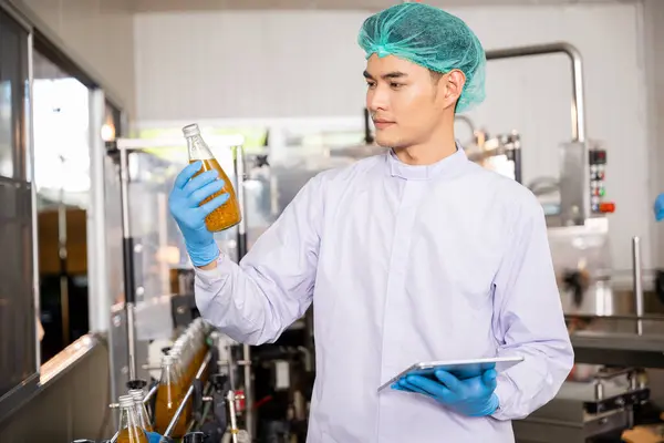 At the beverage bottling factory a quality control officer use tablet to ensure manufacturing line precision machinery engineer inspects and maintains machines for proper basil or chia seed bottling.