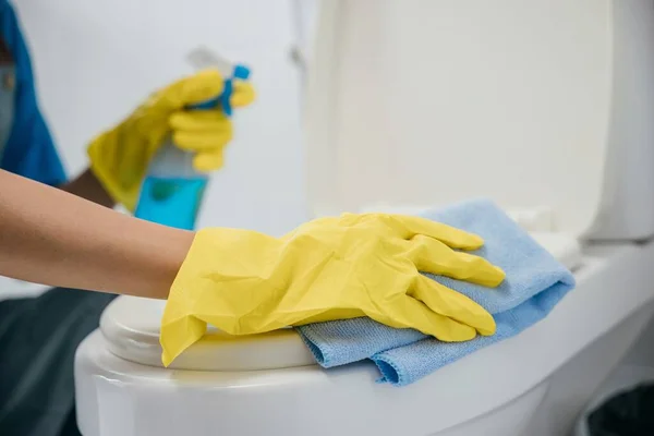 A maid wears yellow gloves meticulously cleaning toilet seat with cloth. Her commitment to hygiene and purity emphasizes housekeeping in the bathroom. Housekeeper healthcare concept