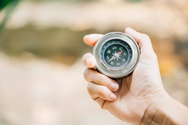 A traveler hand cradles a compass in a park signifying the search for direction and guidance. Amidst nature beauty the compass represents exploration and discovery.