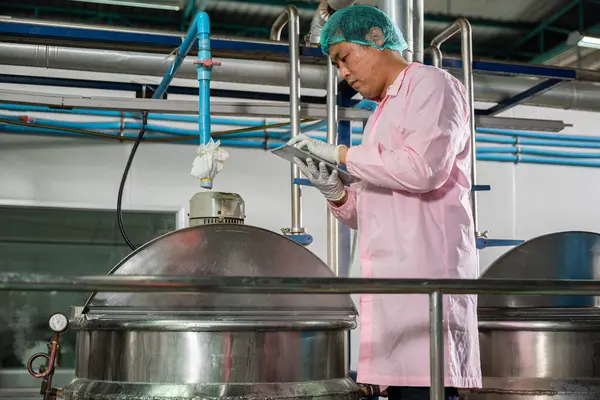 At a beverages factory a worker manages soda water filling with a tablet while an engineer oversees machinery. Quality control ensures industry-leading standards in bottle production.