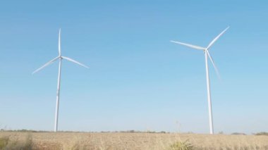 Bir dağ çiftliğinde yel değirmeni türbinleri temiz enerji yeniliğini simgeler. Sürdürülebilir gelişim, mavi gökyüzünün arka planına karşı modern rüzgar teknolojisiyle gelişir..
