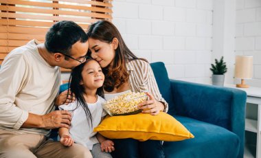 Gülümseyen aile patlamış mısırla televizyon izlerken aile zaman geçirmek eğlence ve mutluluk doludur. Baba, anne, kız ve kardeş gülüşmeler ve neşe paylaşıyor. Evde kaliteli zaman geçirirken güzel anılar yaratıyorlar..