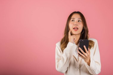 Mutlu bir Asyalı portresi. Güzel, güzel bir kız. Elinde cep telefonu tutarak gülümsüyor ve fikir parmağıyla dokunuşunu düşünüyor.