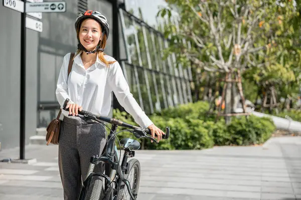 Asian businesswoman morning commute is portrait of cheerfulness. She stands by her bicycle helmeted and suited up embodying modern concept of business commuter where work and outdoor fun coexist.