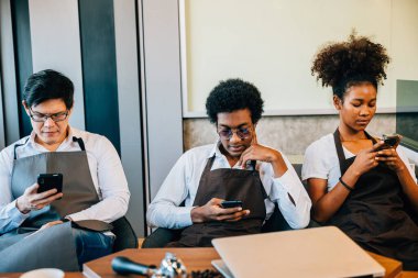 Kafe grubundaki barista ekibi akıllı telefonlara bakıp birlikte dinleniyorlar. Üniformalı profesyoneller telefonla bağlanırken bir anın tadını çıkarıyorlar. Bir kafe ortamında takım çalışması. Emir yok.