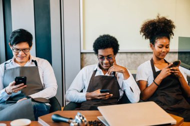 Çeşitli bir grup barmen bir kafede telefonları kullanarak rahatlamanın tadını çıkarıyordu. Üniformalı profesyoneller takım çalışmasını ve akıllı telefon iletişimini benimsiyor. Emir yok.
