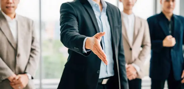 Businessman in suit extends his open palm in gesture of request and handshake, symbolizing trust successful cooperation and teamwork in office setting. It represents professionalism and confidence.