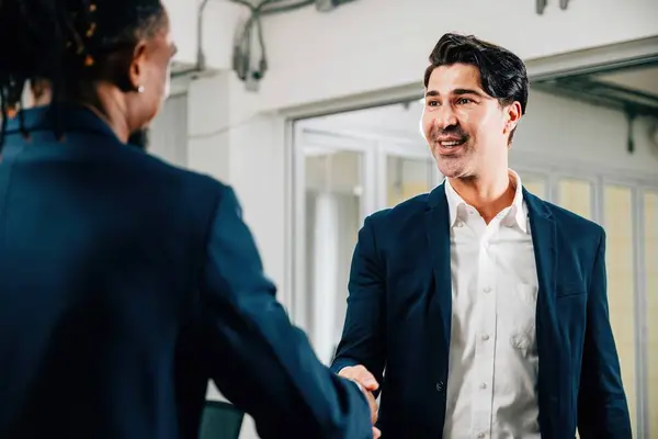 In an office, professionals seal a deal with a handshake, symbolizing their successful collaboration and agreement. Executives, lawyers, and managers celebrate their achievement. Teamwork