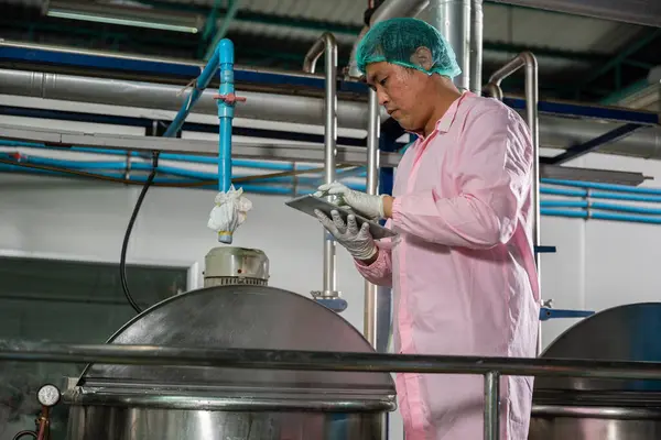 Worker operates a tablet overseeing beverage production while an engineer supervises soda water filling. Emphasizing quality control ensures top-tier standards in bottle manufacturing.