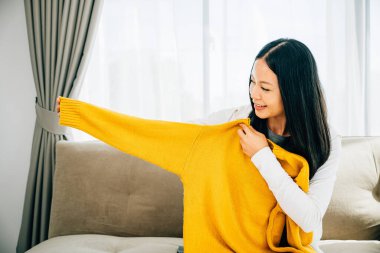 Gülümseyen Asyalı kadın evdeki mutluluktan heyecanlanan bir kutudan gömleğini açıyor. Tatmin olmuş müşteri yeni kıyafetlerini gösteren kutuları internetten açıyor. Teslimat ve online alışveriş konsepti.