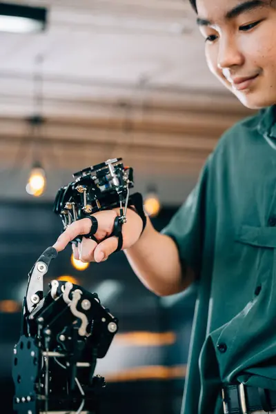Teenage boy in a technical college learns technology testing a robot hand and arm touching fingers for educational skill growth. Embracing futuristic AI and humanity.
