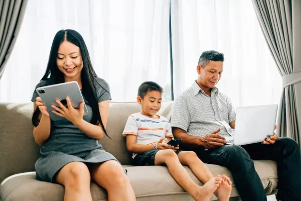 Parents kids engaged with laptops and phones ignoring familial bonding. An Asian familys device dependence portrays the challenges of internet addiction. ignores togetherness