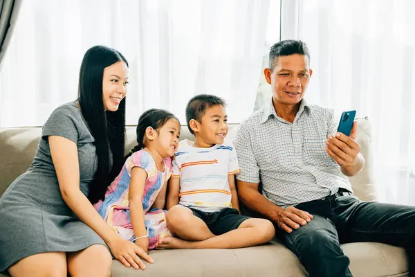 A happy family gathers on a couch kids entertained with a smartphone video parents and children enjoying mobile apps. Illustrating familial joy bonding and technologys role in shared happiness.