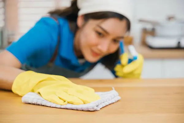 Cleaning service professional wears yellow gloves while cleaning kitchen counter with liquid spray. Housekeeping guarantees home cleanliness and hygiene. Clean disinfect home care. maid household job.