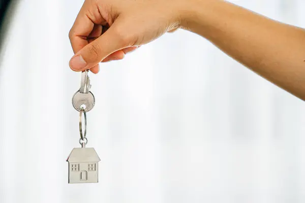 Hand holds key to house marking homeowners achievement. Agent presents model home symbolizing real estate success. Confidence and happiness resonate.