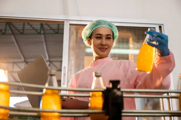 Managerial woman inspects bottles on machinery using laptop in factory. Quality control and liquid check ensure high industry standards. Technology-driven control is the key.