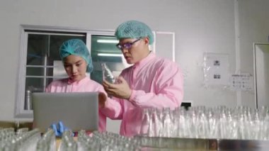 İki mühendis içecek faktörleri taşıma bandında ürün şişe teftişi yapıyor. Kalite kontrol ve teftiş uzmanlar tarafından detaylı analiz için dizüstü bilgisayar kullanılarak izleniyor..