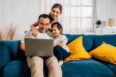 Ebeveynler ve çocuklar dizüstü bilgisayarlarıyla kanepede otururken bir aile evde kaliteli zaman geçirir. Bu modern bağlanma deneyimi hayatlarına neşe ve beraberlik getiriyor..