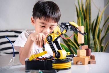 Çocuk tamir etmeyi öğreniyor. Ders kontrol robotu kolu alıyor. Mutlu Asyalı çocuk, evde robotik makine kolu tamir etmek için tornavida kullanıyor.