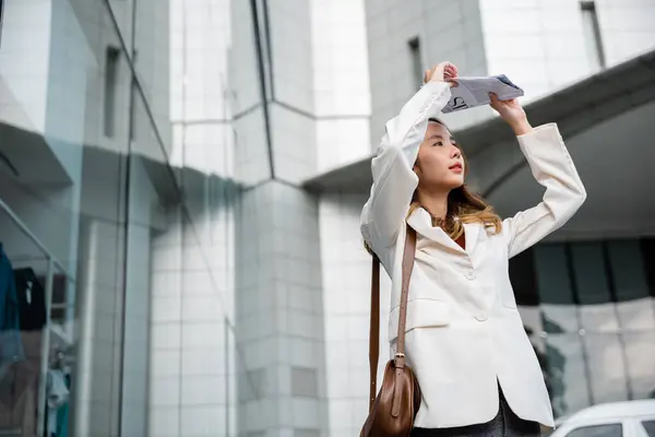 stock image Portrait of Business woman walking out the building after finish work shade sun UV with newspaper. Young Asian woman wearing white shirt while cover the sun by news paper on the streets of downtown