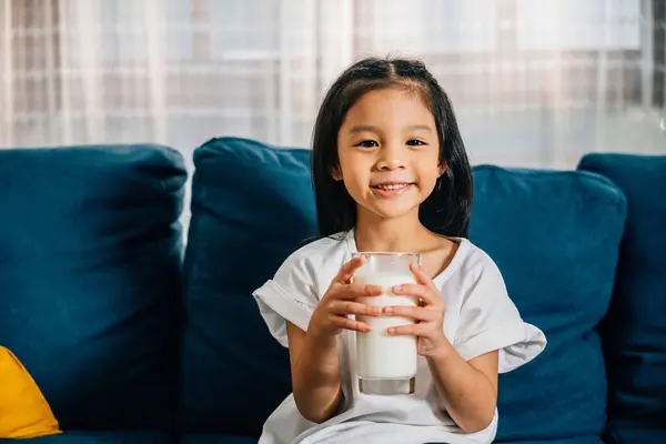 Asiatisk Skolpojke Njuter Ett Glas Mjölk Soffan Som Utstrålar Lycka Royaltyfria Stockfoton
