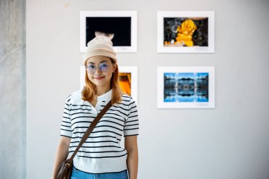 Sanat galerisi önünde gülümseyen ziyaretçi kadın çerçeveli resimlerde beyaz duvarda resimler, Asyalı yaşam tarzı insanların fotoğraf çerçevesinde izledikleri sergi sanat galerisinde yaslandıkları pozlar.