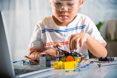 Küçük çocuk oyuncağı monte etmek için tornavidayla cevizi sıkıyor, Asyalı çocuk evde Arduino robot araba ev ödevi yapıyor, eğitim yapay zeka atölyesi dersi öğreniyor.