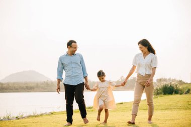 Asyalı bir aile güzel bir bahar parkında yürüyor ve el ele tutuşuyor, doğanın ve birlikteliğin tadını çıkarıyor, mutlu ve neşeli hissediyorlar, mutlu aile günü.