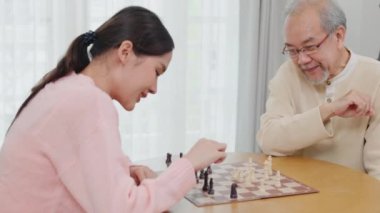 Smiling senior elderly having fun playing chess game with beautiful daughter at home, nurse caregiver in nursing home for leisure, Happy active retired people, Healthcare and medical homecare concept